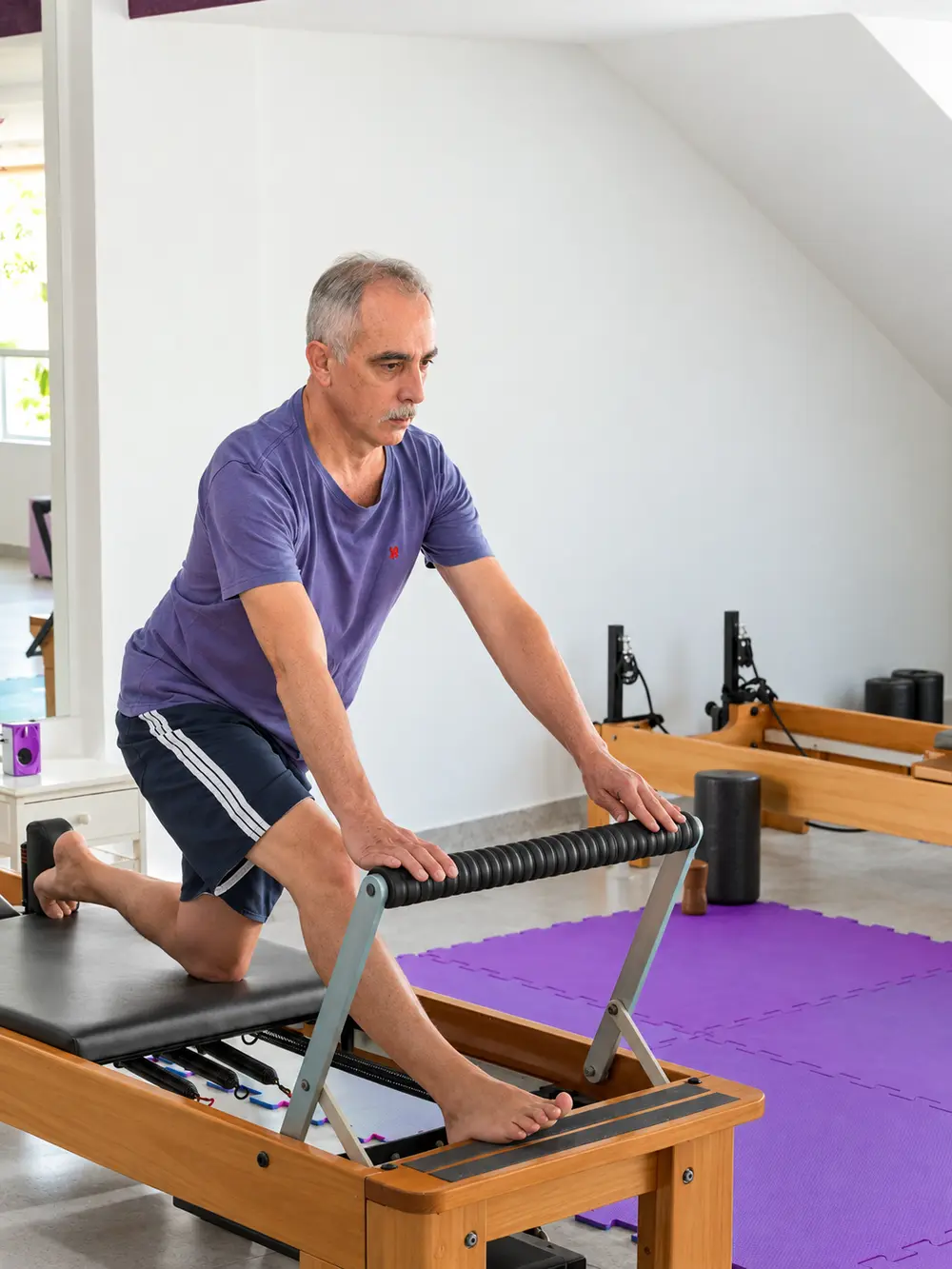 Aluno de cabelos grisalhos fazendo exercício no reformer