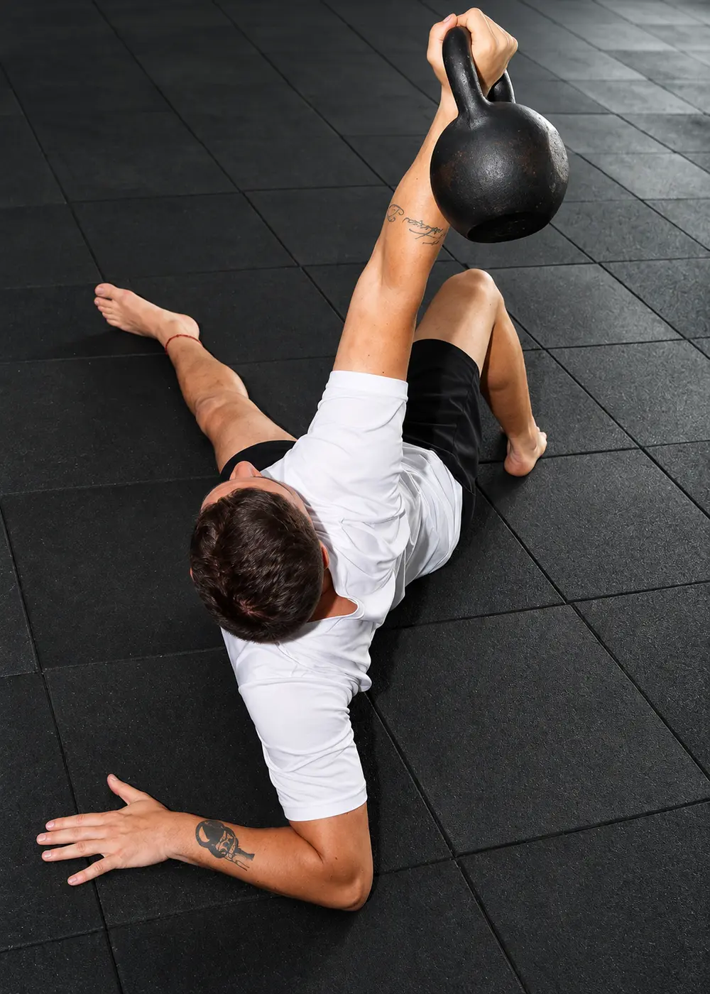Aluno no chão erguendo um kettlebell com o braço estendido