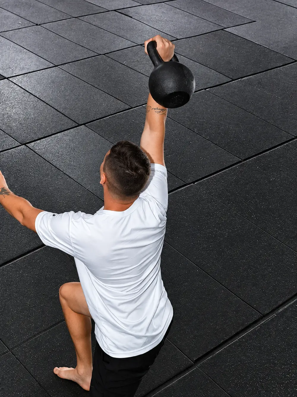 Aluno de costas erguendo o kettlebell acima da cabeça