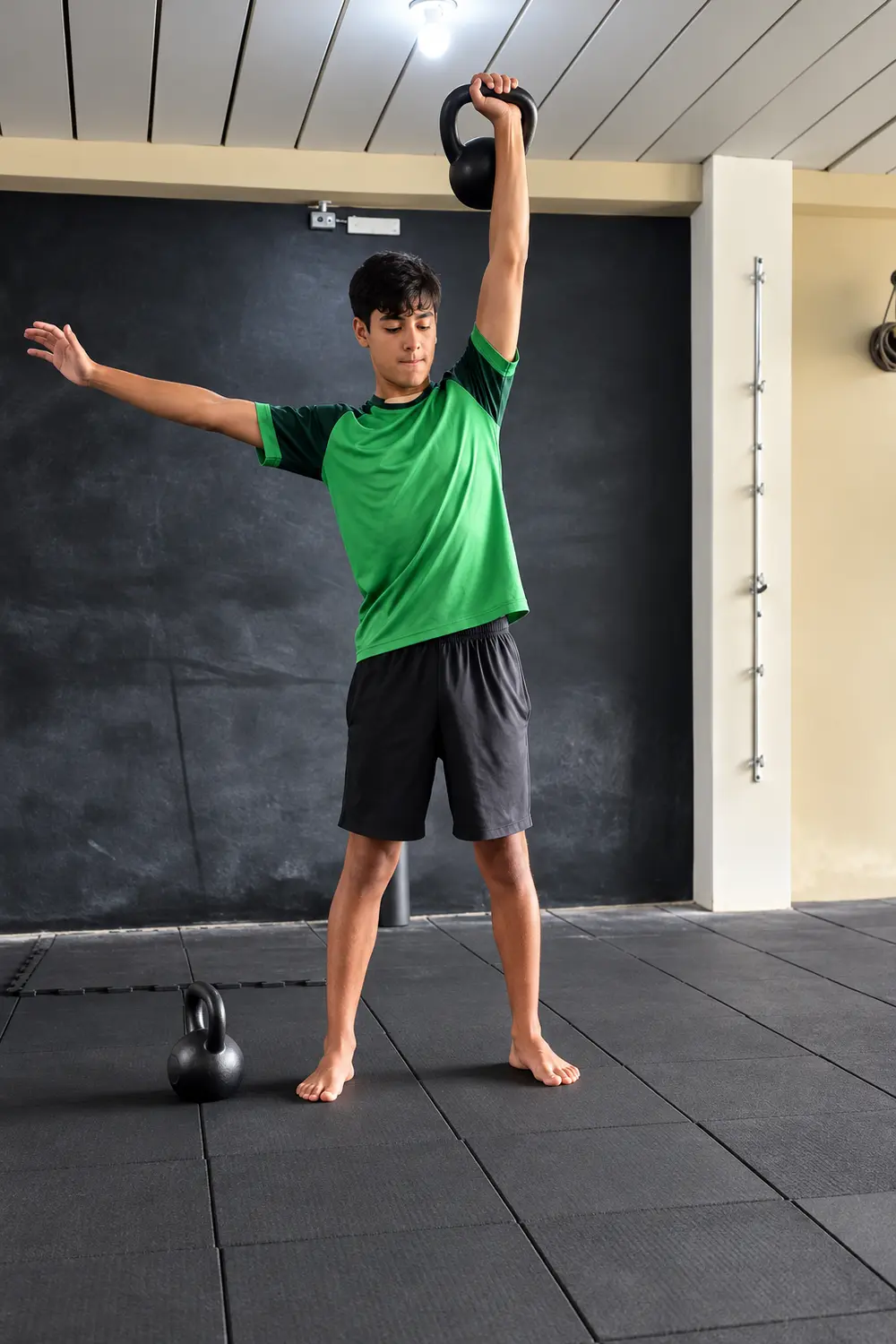 Aluno jovem com o kettlebell erguido e o outro braço aberto