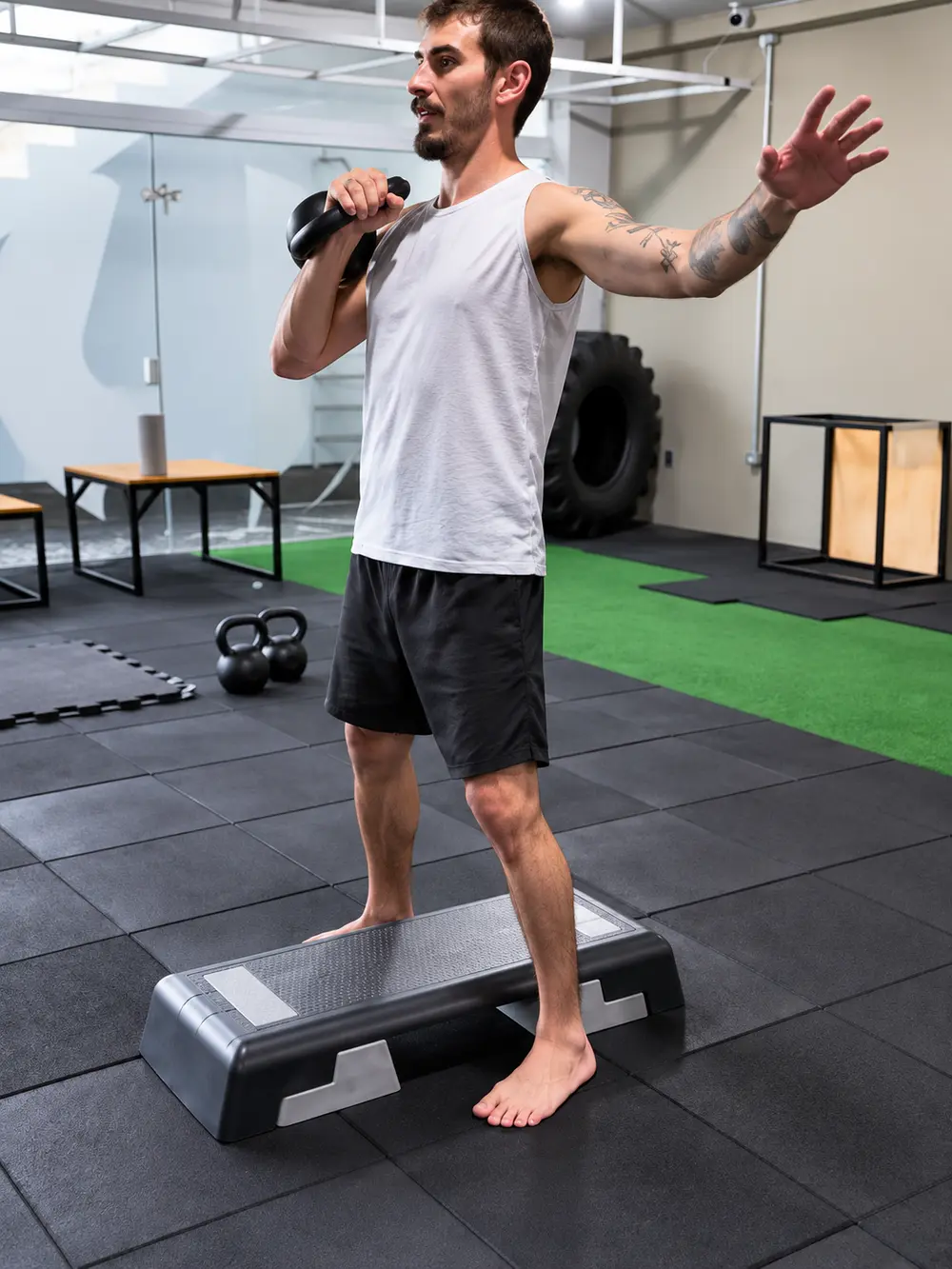 Aluno sobre o step segurando o kettlebell durante o treino